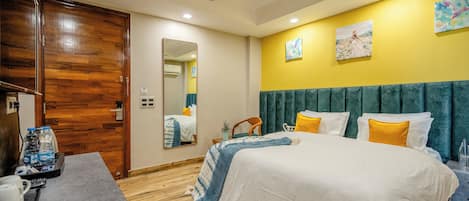A hotel room with a bed, a desk with a telephone and water bottles, a ceiling fan, and artwork on the wall.