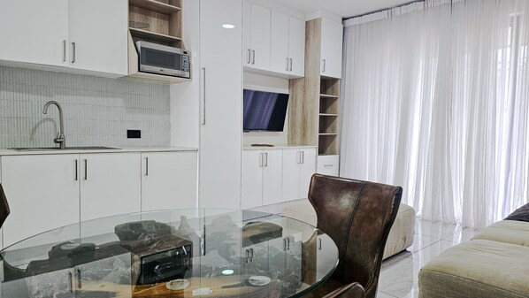 Una cocina moderna con armarios blancos, un microondas y una mesa de comedor de vidrio.