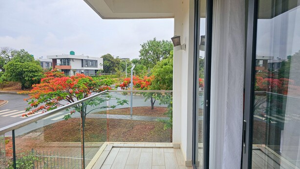 En balkon med gelænder af glas, der giver udsigt over en gade med træer og bygninger.