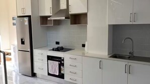Et moderne køkken med hvide skabe, et rustfrit stål køleskab, indbygget ovn og et glas spisebord.