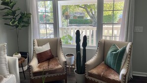 A living room with two armchairs, a white sofa, and a large window with a view of a house and trees.