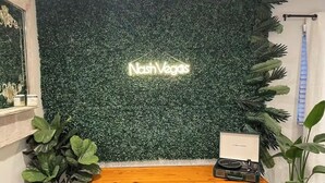 A reception desk with a neon sign reading "Nash Vegas" against a green foliage backdrop.