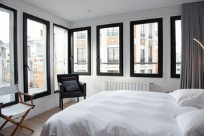 Una camera d'albergo con un letto grande, una sedia e numerose finestre che offrono vista sulla città.
