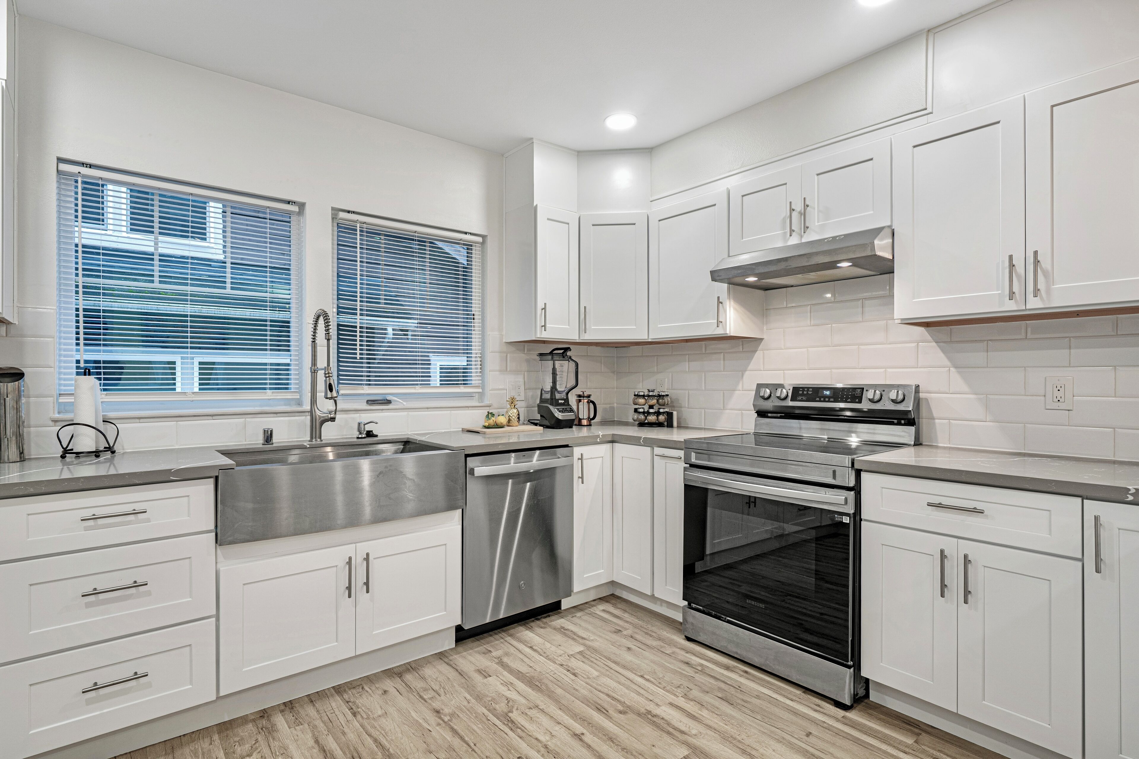 A modern kitchen with white cabinets, stainless steel appliances, and a wooden floor.