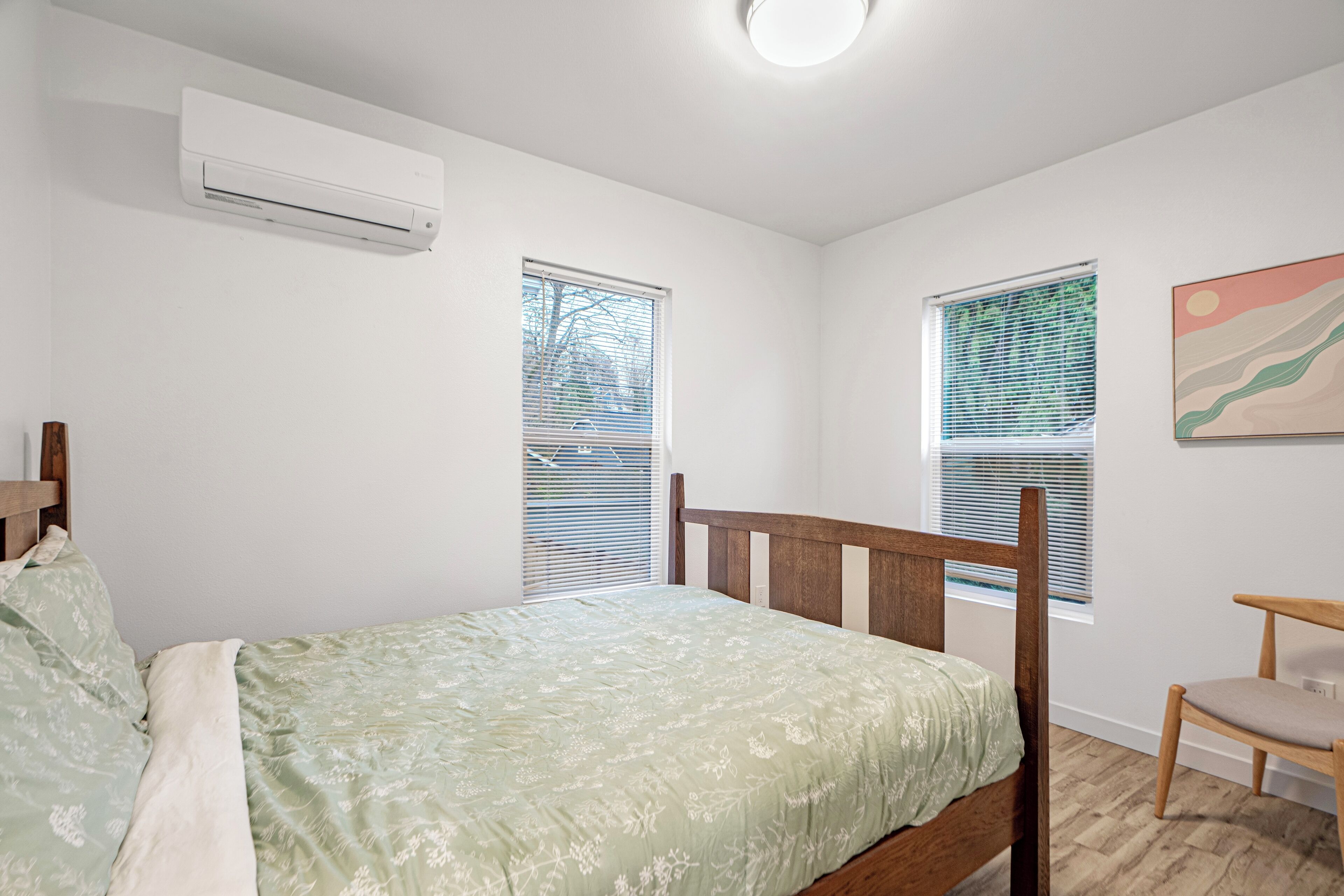 Un dormitorio con una cama, cabecera de madera, una silla y dos ventanas con persianas.