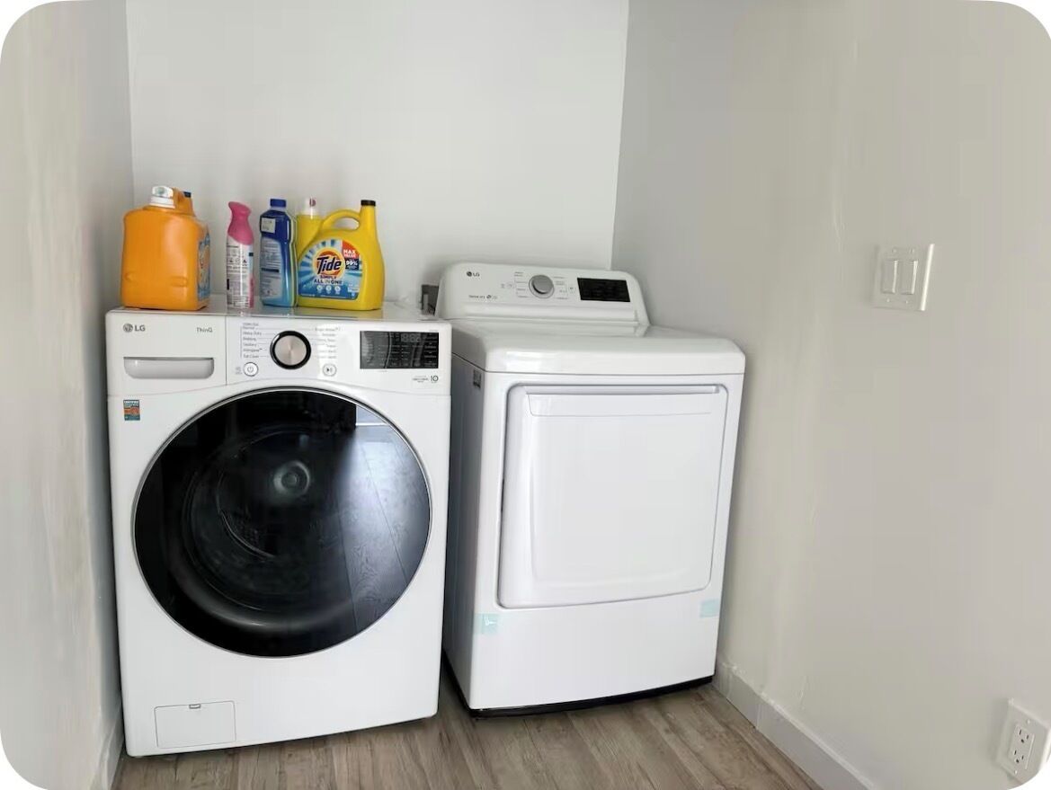 Une buanderie équipée de deux machines à laver et de différents bidons de lessive.