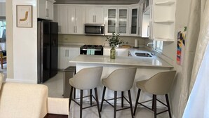 Una cocina moderna con armarios blancos, una isla central con taburetes altos, un ventilador de techo y un equipo de aire acondicionado.