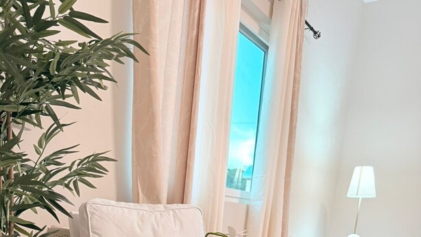 Una habitación con un sofá blanco, una mesita de madera con una planta, una lámpara y una cama con colcha blanca.