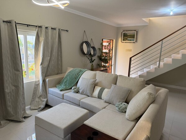A living room with a beige sofa, a matching ottoman, and a staircase. - 3-bedroom townhome in amazing Ocho Rios with Pool access, Private Gazebo,Balcony (Ocho Rios)