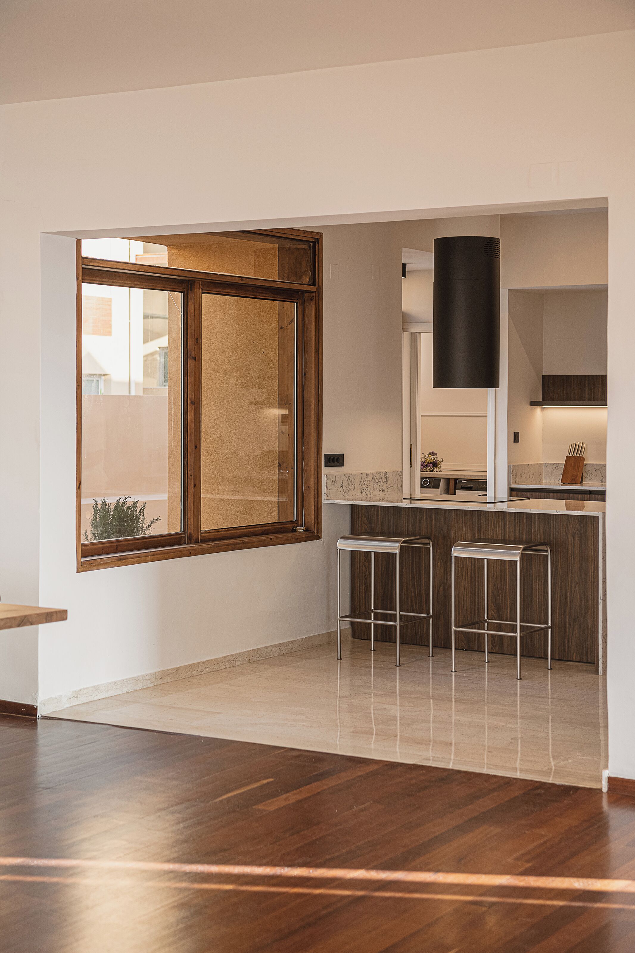 A modern kitchen with a large window, wooden bar stools, and a central island.