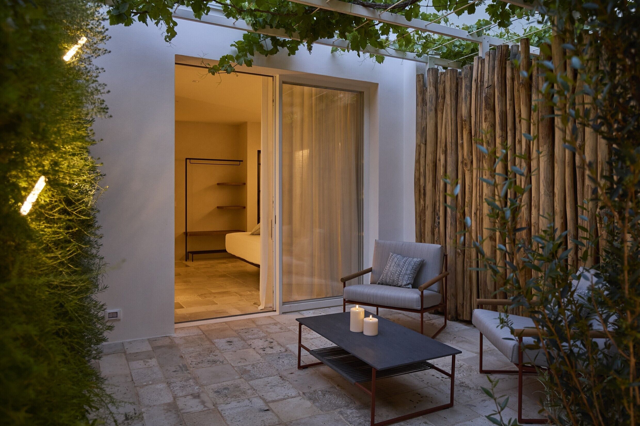 Un patio al aire libre con un sofá, una mesa con velas y una puerta corrediza de vidrio que da a un dormitorio.