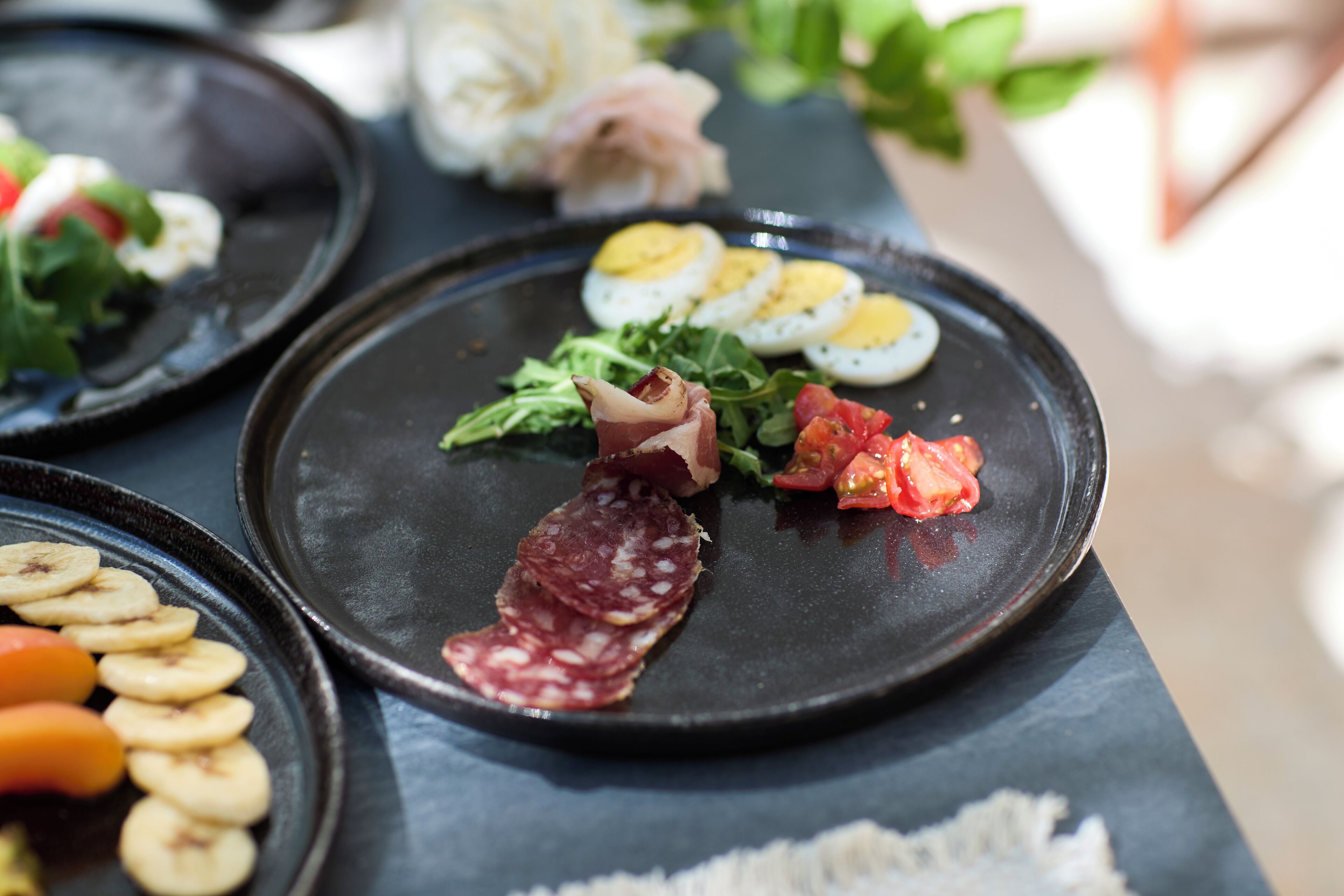 Una mesa con platos de comida que incluyen salami en rodajas, huevos y verduras.