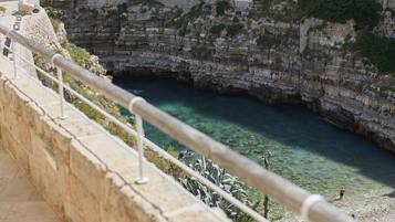 A coastal view with a clear blue sea, rocky cliffs, and a stone railing.