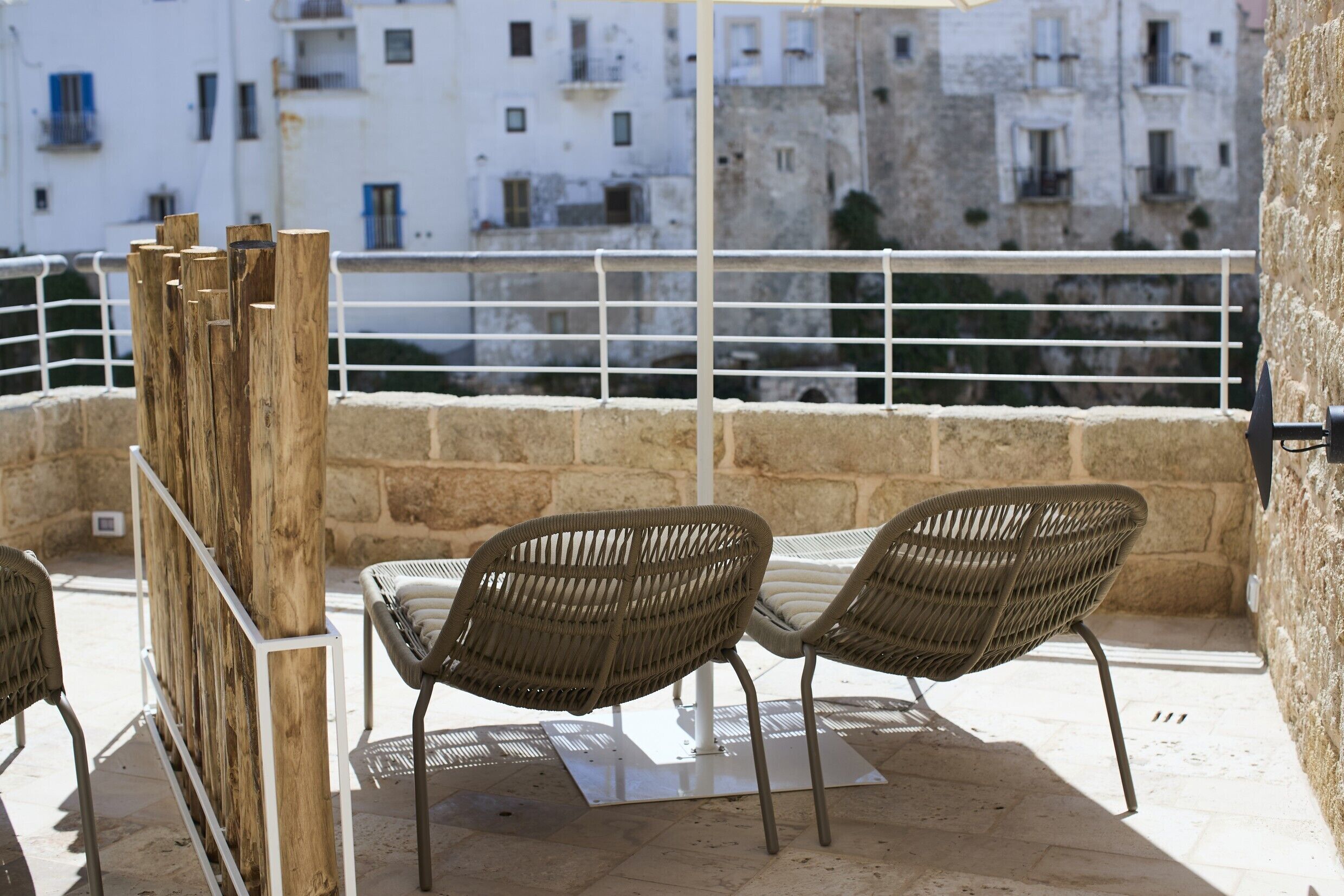 An outdoor seating area with wicker chairs and a table, overlooking a cityscape with stone buildings.