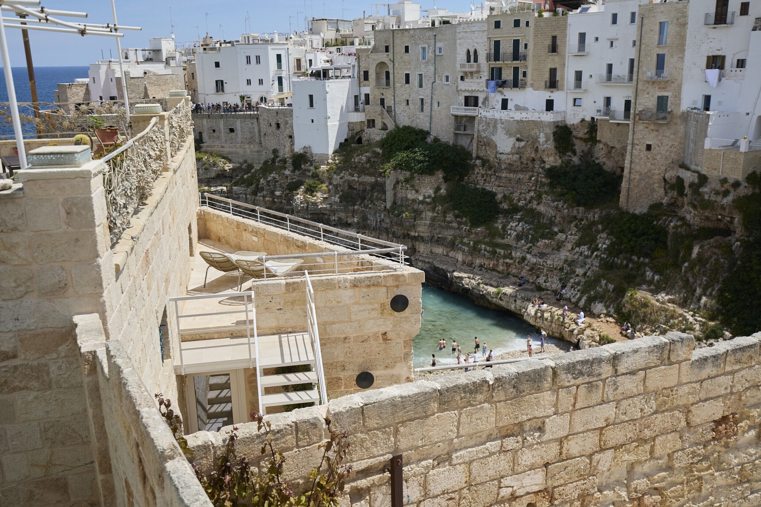 A coastal town with stone buildings, a rocky cliff, and a clear blue sea.