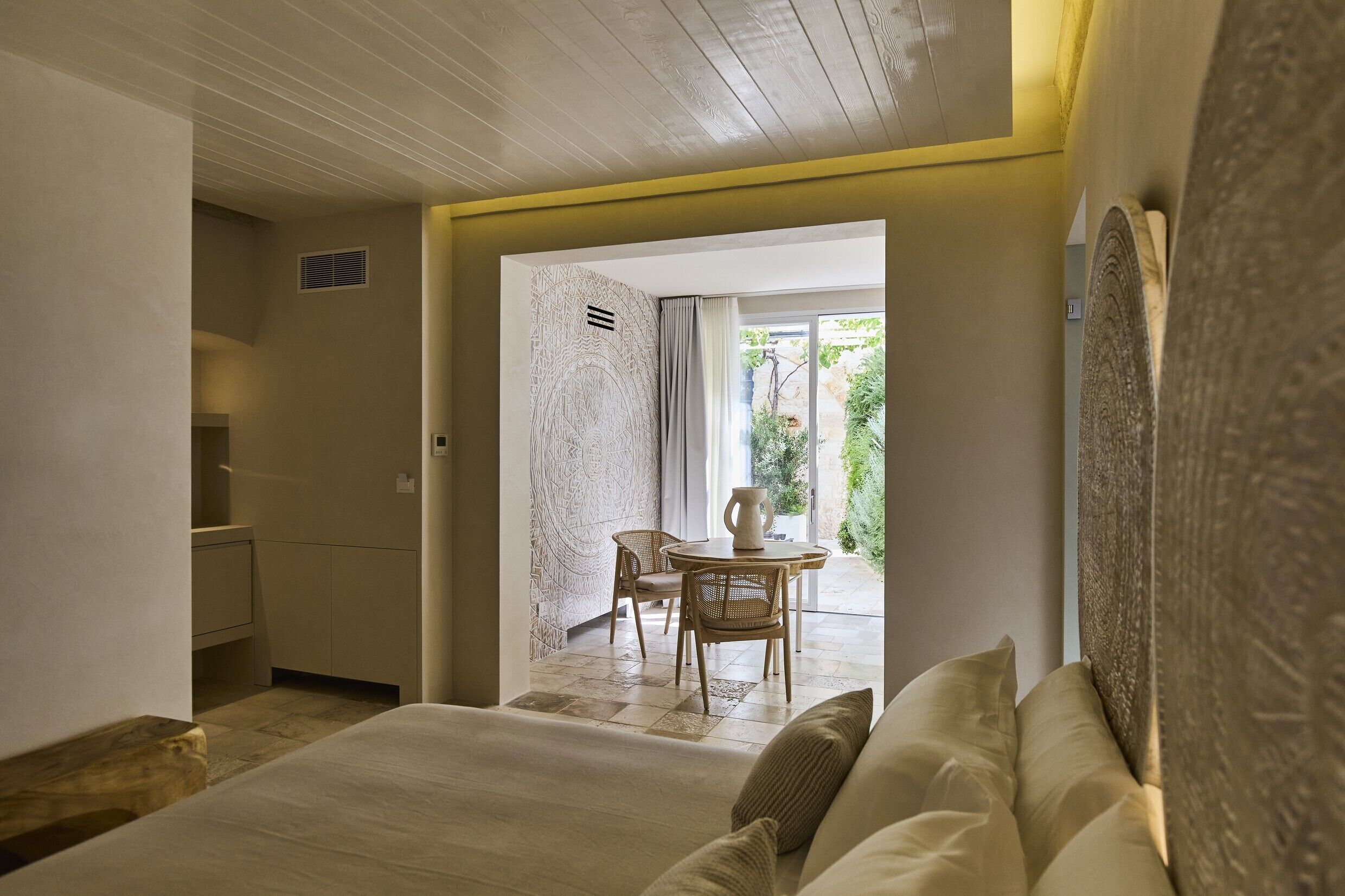 A hotel room with a bed, a sitting area with a table and chairs, and a view of the outdoors.