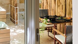 A dining area with a wooden table set for two, surrounded by chairs, and a stone wall in the background. - Musae In Lama (Polignano a Mare)