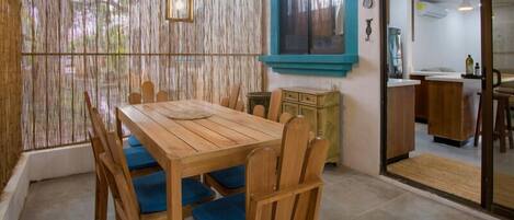 Une table de salle à manger en bois, agrémentée de coussins bleus, un paravent en bambou tressé et une fenêtre encadrée de bleu-vert.