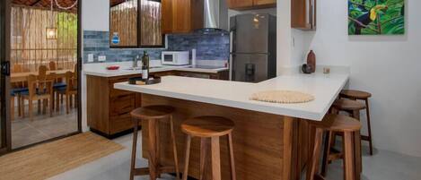 Une cuisine moderne dotée d’un îlot central, de tabourets en bois, d’un réfrigérateur et d’un four à micro-ondes.