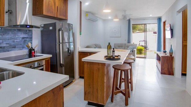 Una cocina moderna con una isla central, armarios de madera, electrodomésticos de acero inoxidable y una zona de comedor con taburetes.