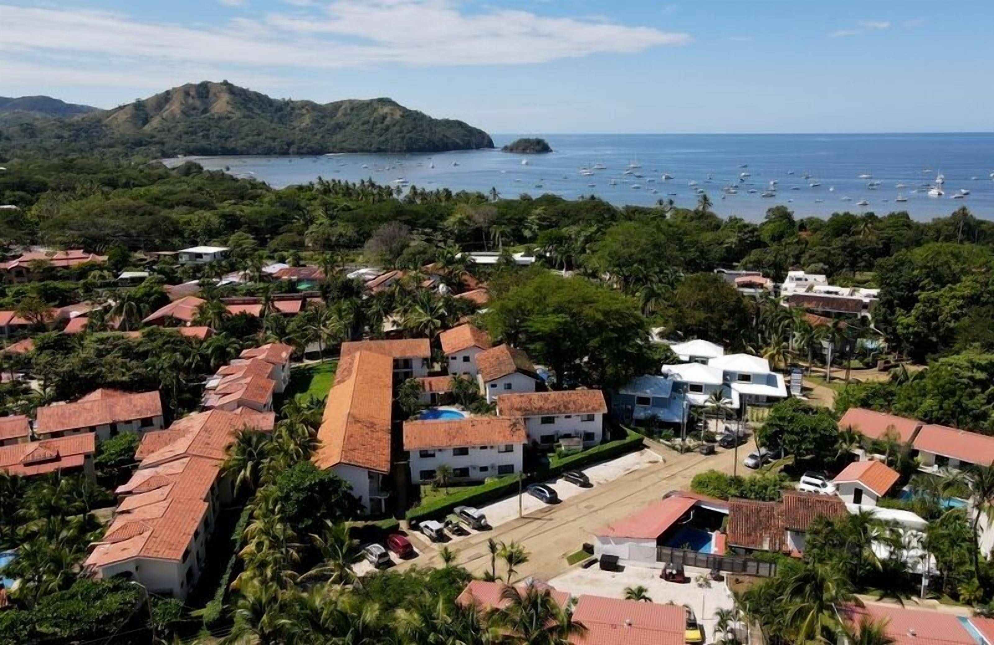 A coastal residential area with houses, a swimming pool, and boats in the background.