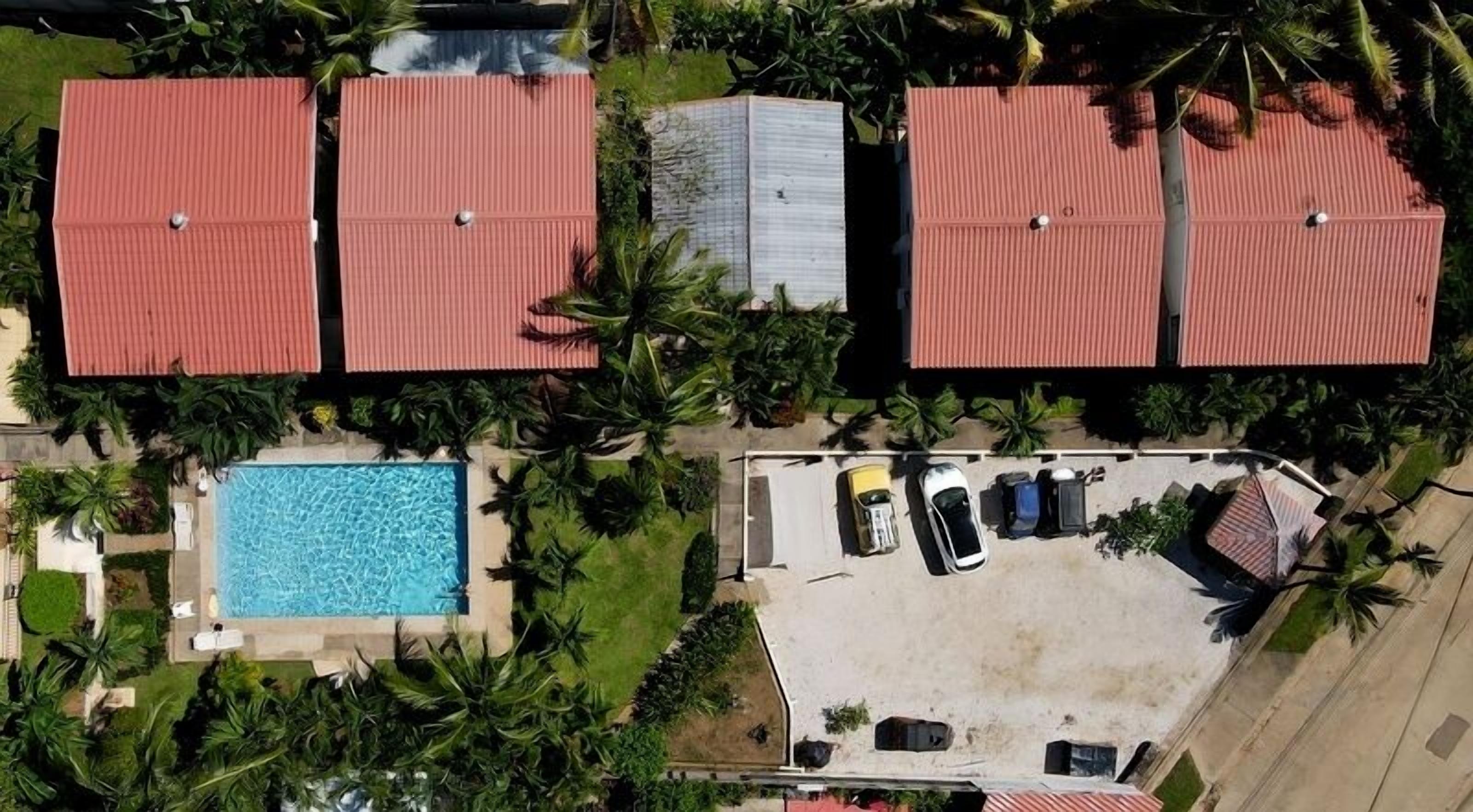 Ein Wohngebiet mit vier Gebäuden mit roten Dächern, einem Schwimmbad und einem Parkplatz mit Autos.