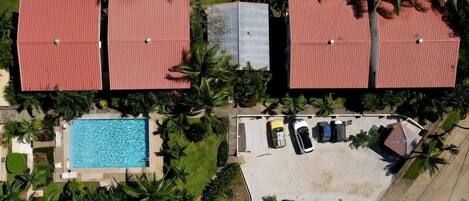 A residential area with four red-roofed buildings, a swimming pool, and a parking area with cars.