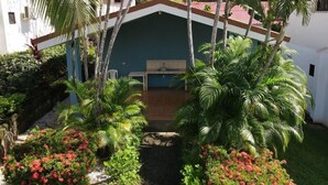 Un espacio exterior techado con un banco de madera, rodeado de abundante vegetación y palmeras.