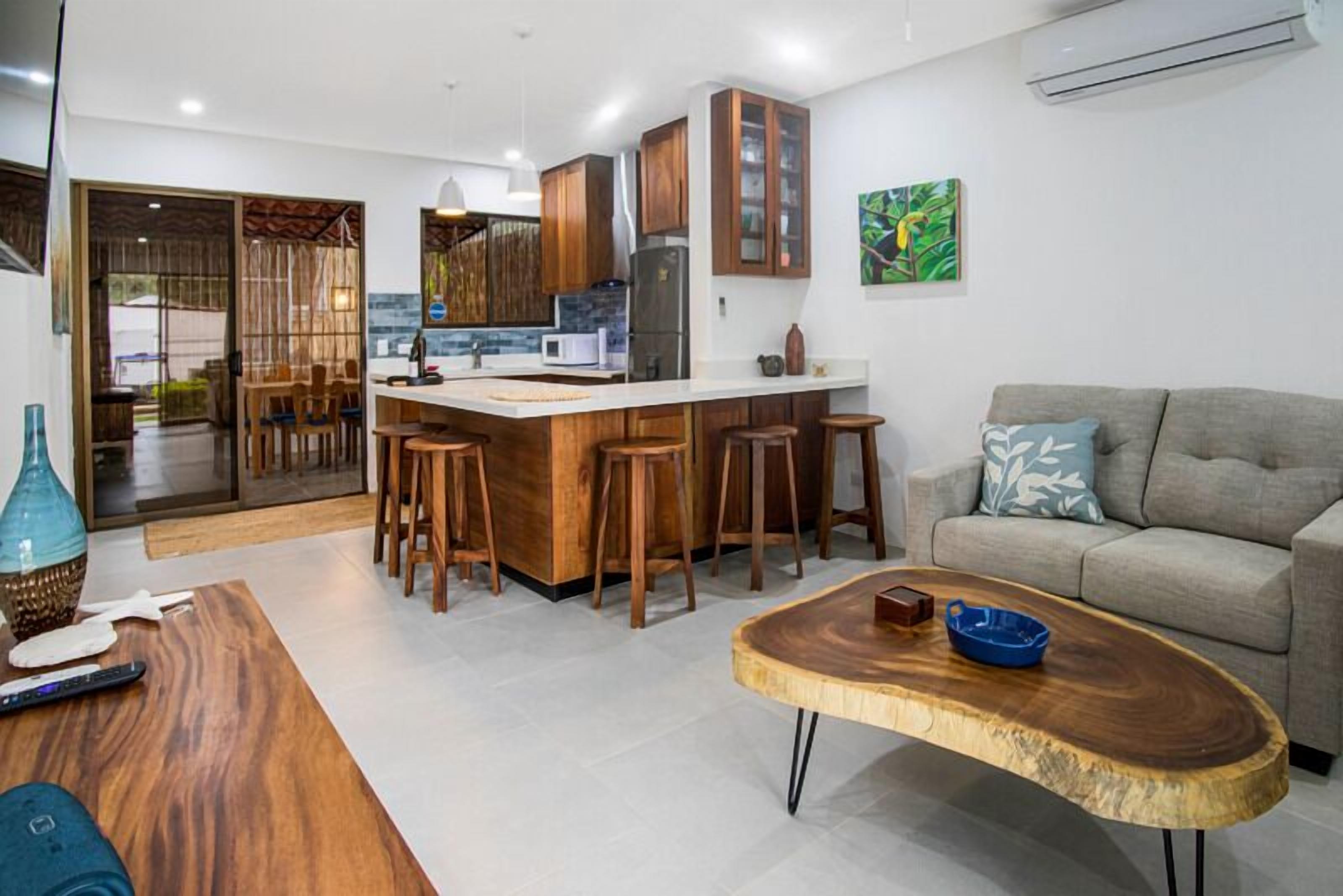 Una cocina moderna con armarios de madera, una isla central con taburetes y una zona de comedor con mesa de madera.