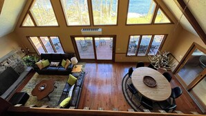 Un loft amplio con techo alto, ventanas grandes que ofrecen vistas a un lago, chimenea, zona de comedor y rincón de estar acogedor.