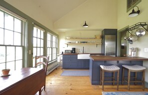 A kitchen with a wooden table, chairs, a built-in island with stools, and a refrigerator.