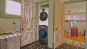 A laundry room with a washing machine, a sink, and a door leading to another room.
