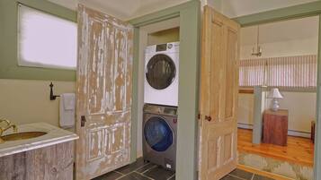 A laundry room with a washing machine, a sink, and a door leading to another room.