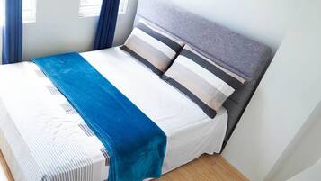 A neatly made bed with a striped bedspread, a blue throw blanket, and a grey headboard.