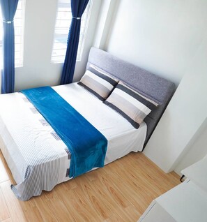 Una cama bien tendida con una colcha a rayas, un plaid azul y un cabecero gris.
