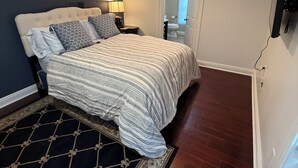 A bedroom with a bed, nightstands, a lamp, a TV mounted on the wall, and a door leading to a bathroom. - Charming 2-bedroom 2 1/2 bath House with WiFi and AC in fabulous Cincinnati (Cincinnati)