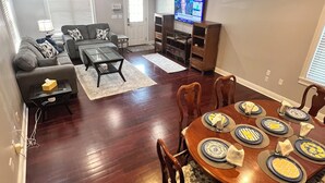 A spacious living room with a dining area, a flat-screen TV mounted on the wall, and a large window with blinds. - Charming 2-bedroom 2 1/2 bath House with WiFi and AC in fabulous Cincinnati (Cincinnati)