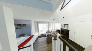 A spacious living area with a high ceiling, a fireplace, a sofa, and a view of the outdoors through large windows. - Artistic Hillside Loft (Blue Mountain)