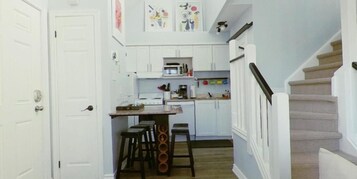 Un pasillo estrecho con una zona de cocina que incluye armarios blancos, una estufa y taburetes de bar.