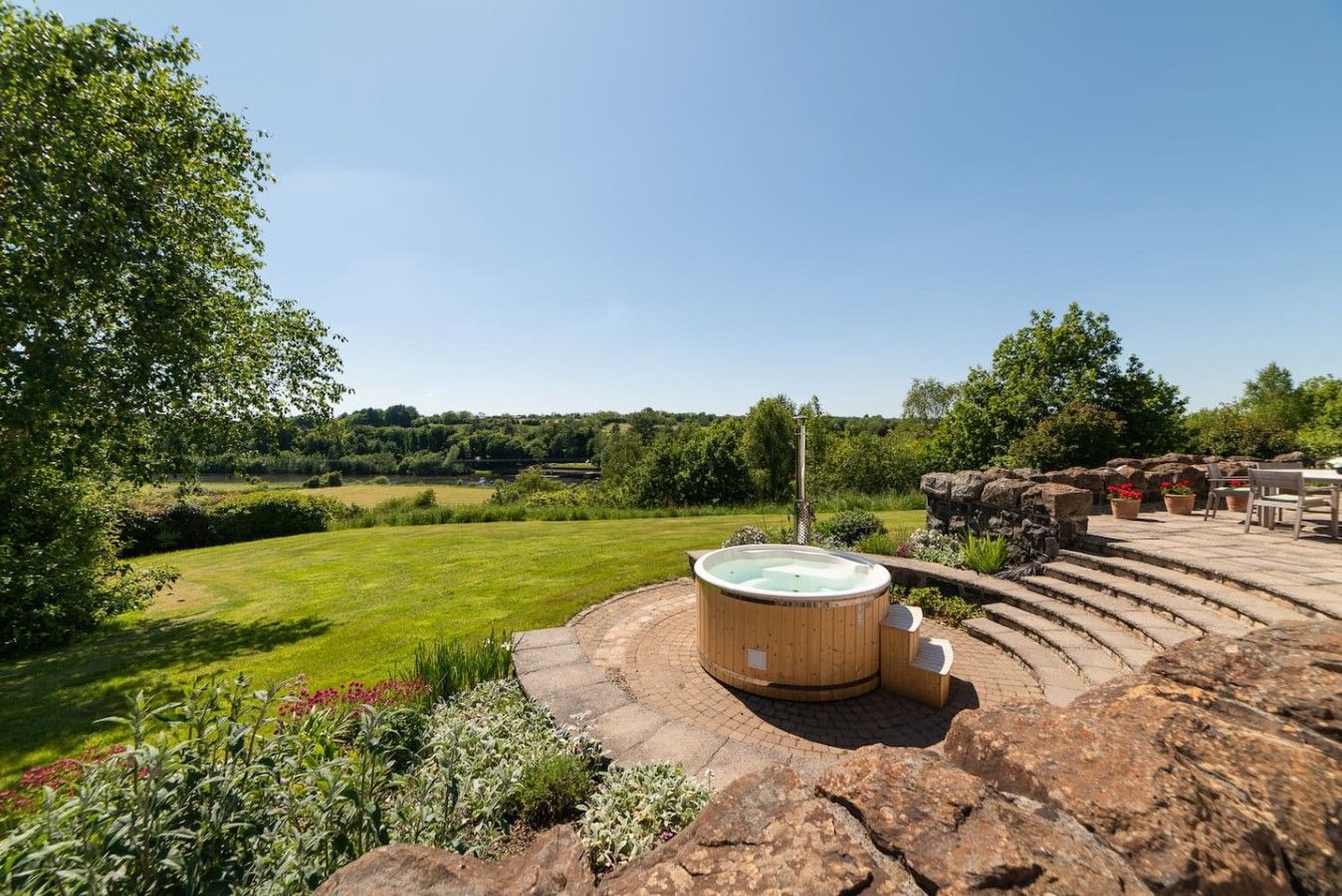 Un jacuzzi en un jardín con una zona de estar de piedra y vistas al campo.