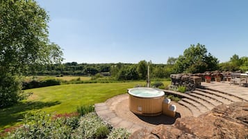 Un jacuzzi en un jardín con una zona de estar de piedra y vistas al campo.