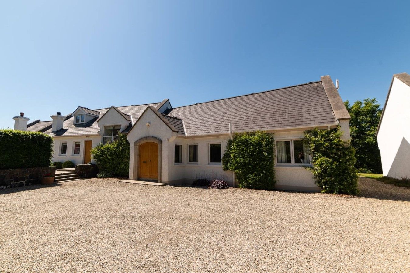 A residential property with a gravel driveway, a central entrance with a wooden door, and a symmetrical design with multiple chimneys.