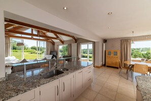 A modern kitchen with granite countertops, a built-in sink, and a dining area with a table and chairs. - Stunning North Coast Villa, River View Hot Tub 20+ (Coleraine)