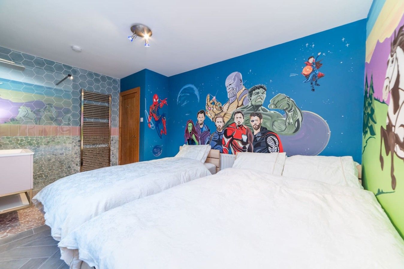 Een slaapkamer met twee bedden, een muurschildering en een badkamer met douche.