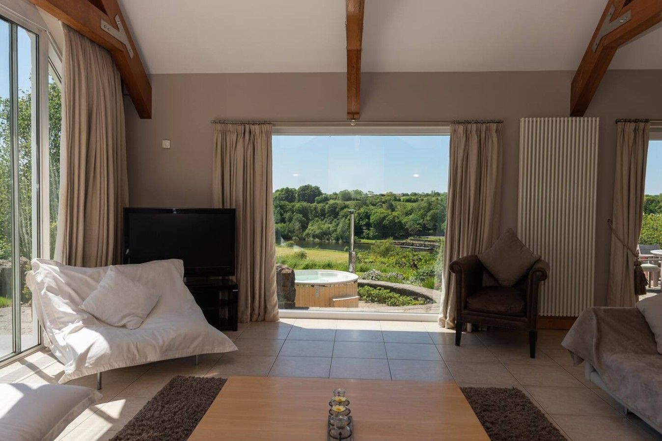 Amplia sala de estar con televisor, dos sofás, una mesa de centro y vistas a un jacuzzi y follaje exterior.