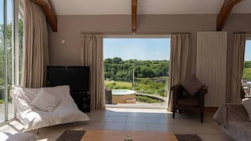 Amplia sala de estar con televisor, dos sofás, una mesa de centro y vistas a un jacuzzi y follaje exterior.