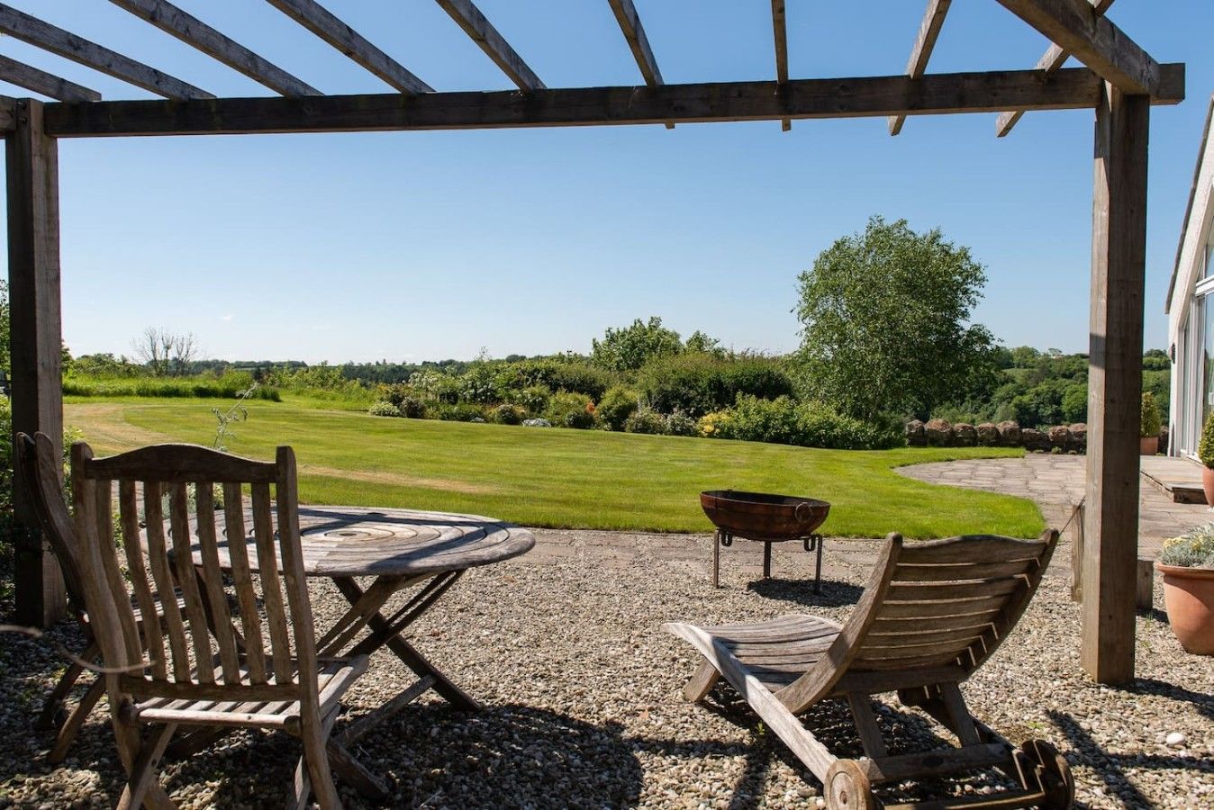 Un área de estar exterior con mesa y sillas, una parrilla y vistas a un césped y jardín bien cuidados.