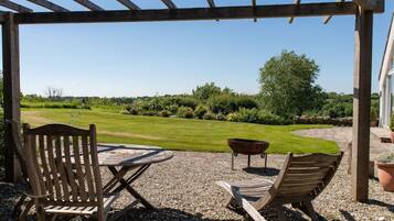 Un área de estar exterior con mesa y sillas, una parrilla y vistas a un césped y jardín bien cuidados.