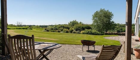 An outdoor seating area with a table and chairs, a barbecue grill, and a view of a well-maintained lawn and garden.