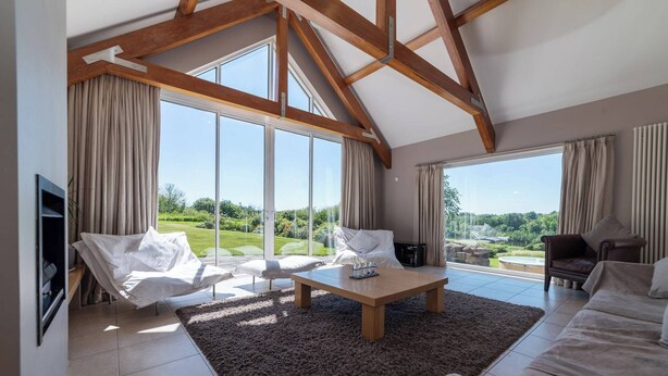 A spacious living room with a high ceiling, large windows, and a view of a lush garden.